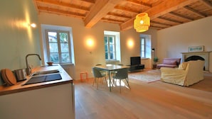 A spacious living area with a wooden ceiling, a dining table with chairs, a sofa, and a fireplace.