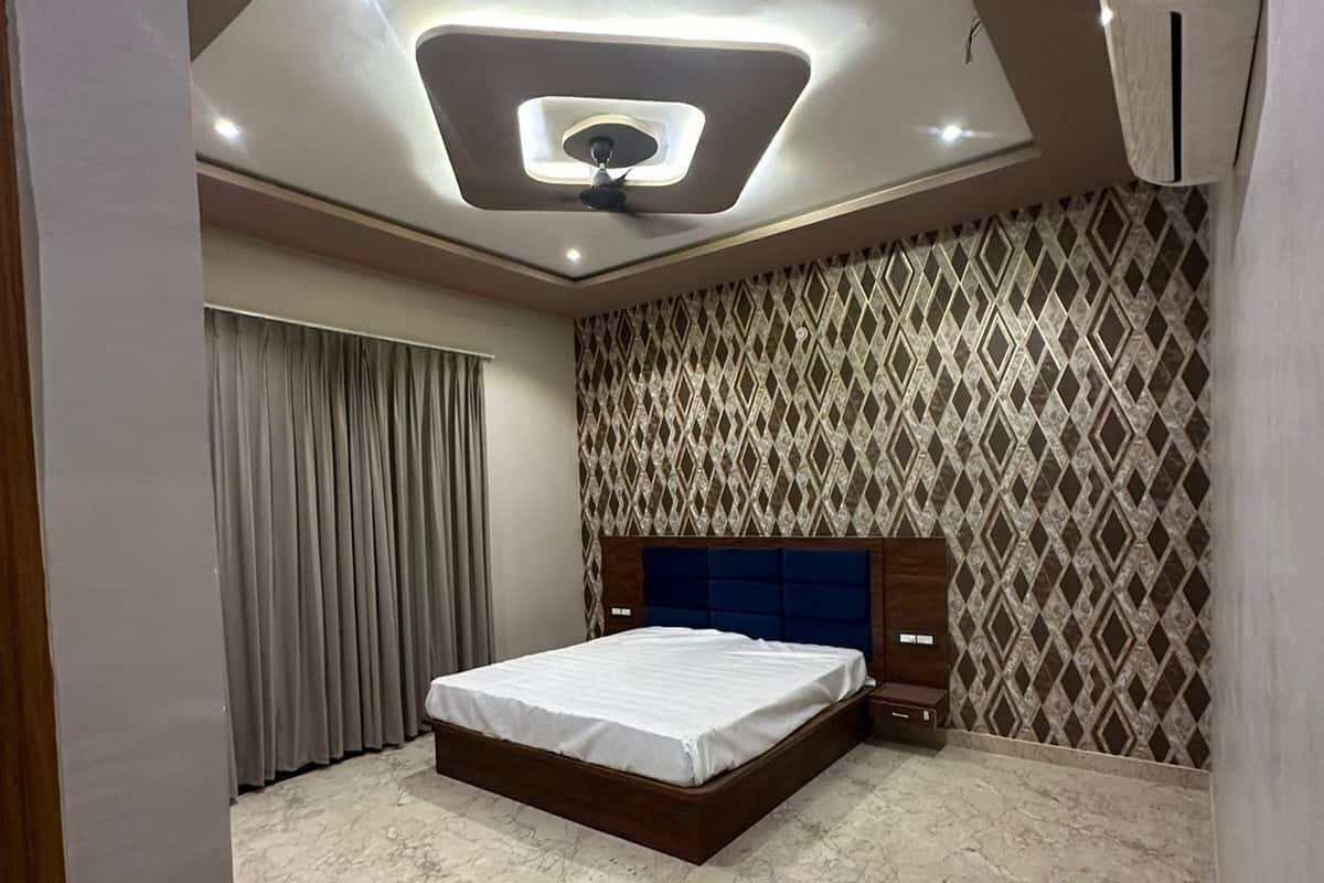 A modern bedroom with a central bed, marble flooring, patterned wallpaper, and a ceiling light fixture.