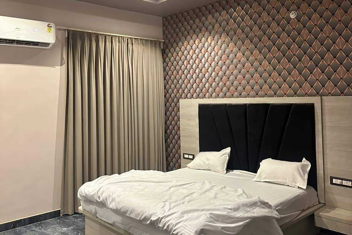 A modern hotel room with a large bed, a ceiling fan, an air conditioning unit, and a patterned wall.