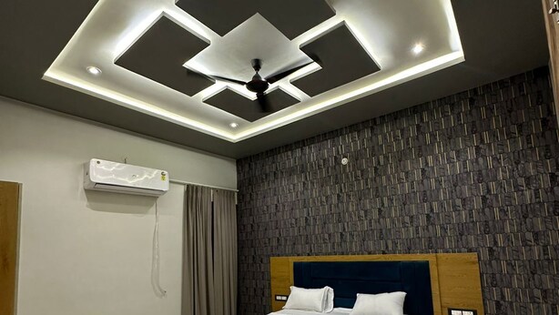 A modern bedroom with a central bed, a ceiling fan, recessed lighting, a textured wall, and a built-in air conditioning unit. - The Black Eagle Resort (Pushkar)