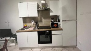 Een kleine keuken met witte kastjes, een magnetron, een koffiezetapparaat en een vaatwasser.