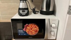 Een magnetron met een digitaal display, een koffiezetapparaat en een waterkoker erop.