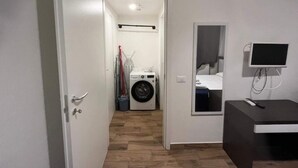 Een hotelkamer met een wasmachine, een spiegel, een televisie en een bureau.