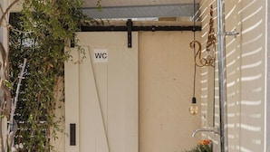 Passadís exterior estret amb un senyal de WC, una làmpada penjant i una petita jardini amb flors.