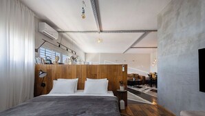 Un dormitori modern amb un llit gran, un panell de capçal de fusta i vista a una zona de menjador.