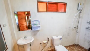 Ein kleines Badezimmer mit einem weißen Waschbecken, einer Toilette und einem Spiegel über dem Waschbecken. Ein Ablagefach mit Pflegeprodukten und ein Fenster über dem Spiegel sind vorhanden.