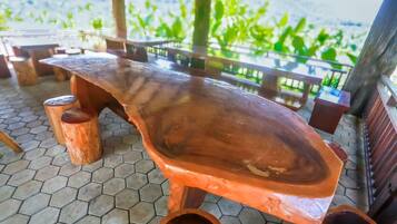 A wooden table with a unique curved design, supported by cylindrical legs, set on a hexagonal tile floor.