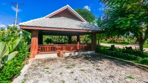 Ein Gazebo mit einem Ziegeldach und Holzgeländer, umgeben von üppiger Vegetation.