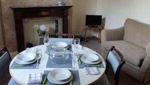 A dining area with a round table set for four, a fireplace, and a television in the background.