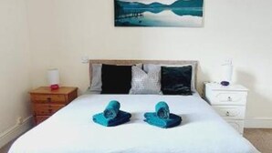 A bedroom with a bed, pillows, a nightstand, a lamp, and a painting on the wall.