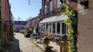 A narrow cobblestone street with outdoor seating and a building with a green awning.
