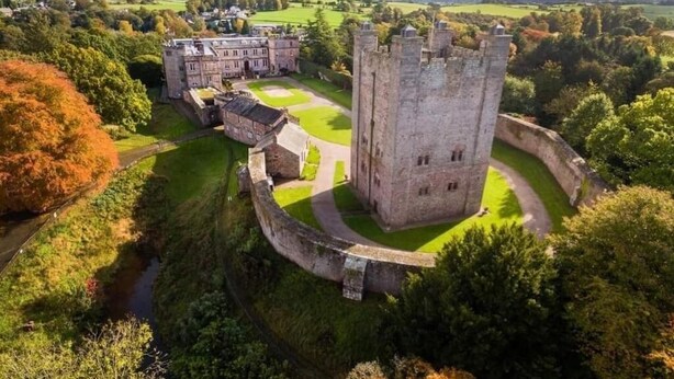 A castle with a large tower, surrounded by a moat and lush greenery.