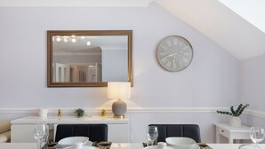 Een eetgedeelte met een witte tafel, zwarte stoelen, een spiegel, een klok en een lamp.