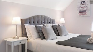 Een net opgemaakt bed met een gestoffeerd hoofdbord, twee nachtkastjes met lampen, en een wand met een poster.