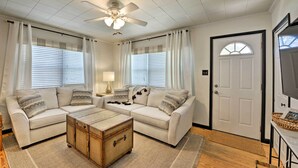 A living room with two white sofas, a wooden chest, and a ceiling fan.
