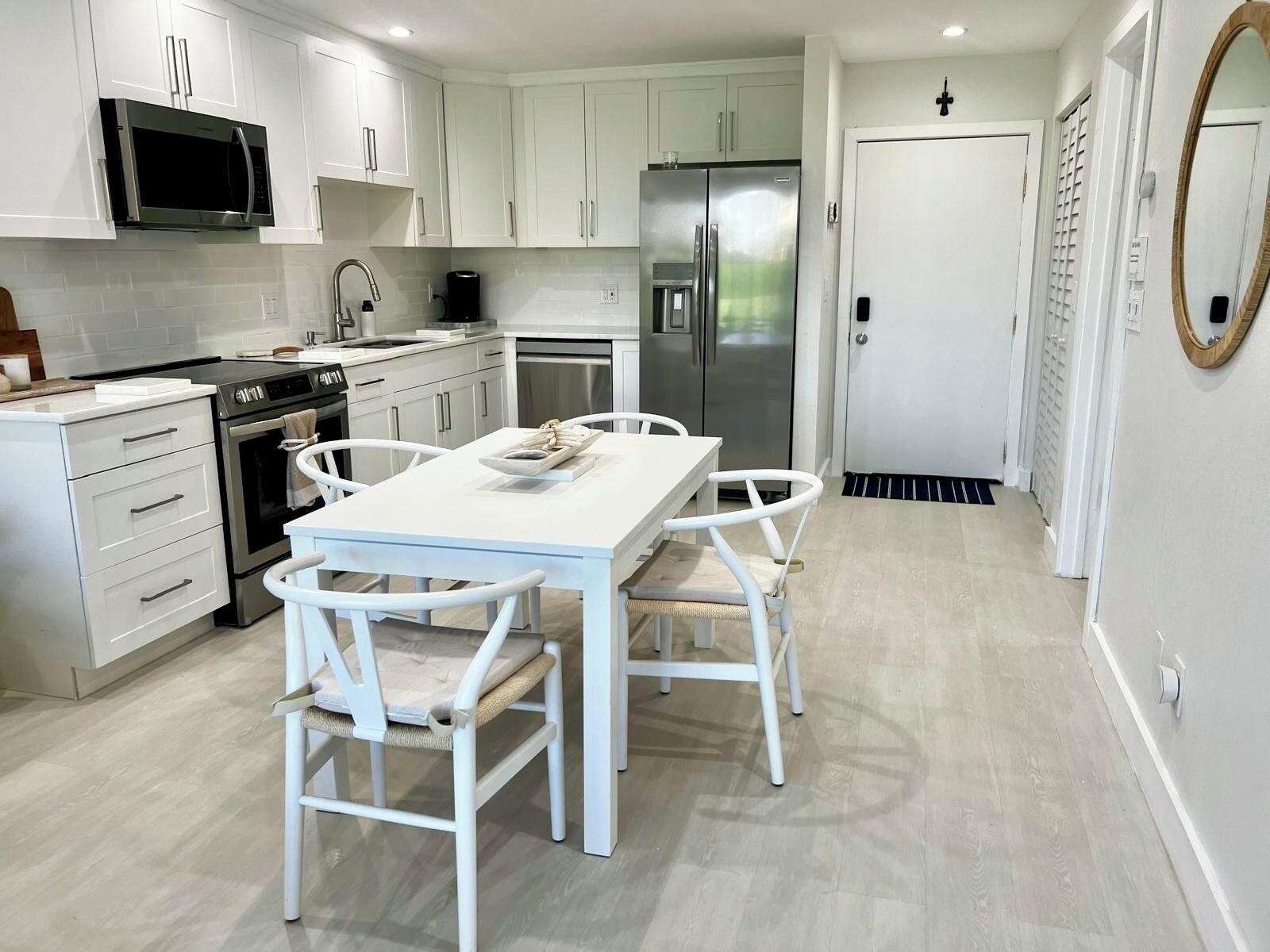 A modern kitchen with white cabinetry, stainless steel appliances, and a dining area with a white table and chairs.