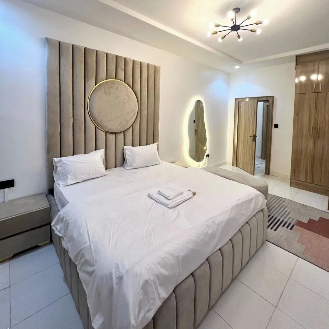 A modern bedroom with a large bed, a round mirror, and a wardrobe.