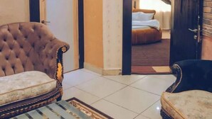 A hotel room with a tufted armchair, a sofa, a bed with a striped bedspread, and a view through an open door. - Top Ranks Hotel Galaxy (Yenagoa)