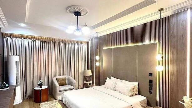 A modern bedroom with a large bed, a side table, a chair, and a ceiling fan. - Top Ranks Hotel Galaxy (Yenagoa)