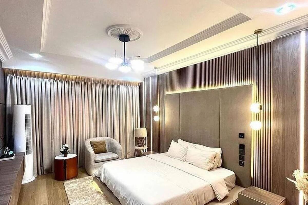 Quarto moderno com uma cama grande, uma mesinha de cabeceira, uma cadeira e um ventilador de teto.