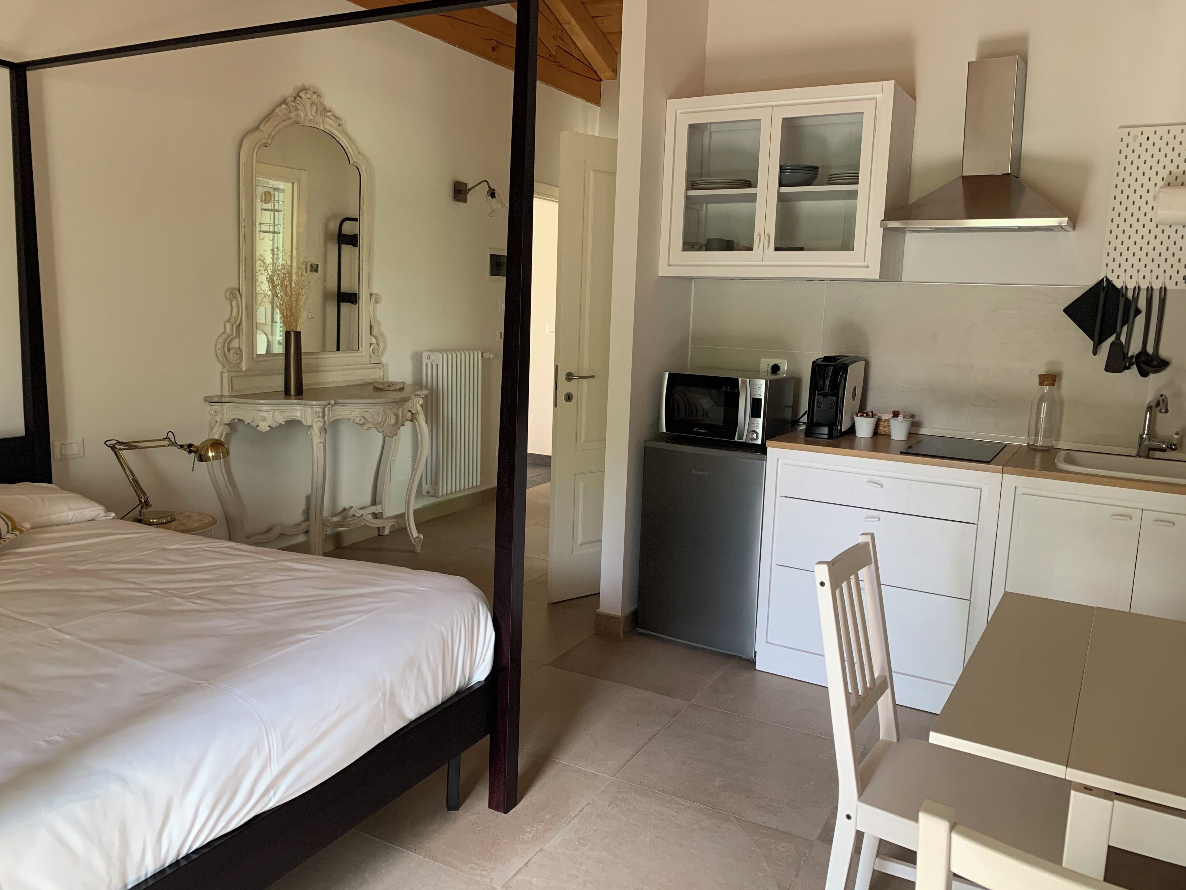 Une chambre à coucher avec un lit à baldaquin, une table de chevet avec une lampe et un miroir. À côté de la chambre, se trouve une petite cuisine équipée d’un four à micro-ondes, d’un grille-pain et de placards.