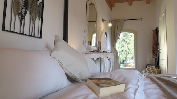 Un dormitorio con cama, mesita de noche, espejo y ventana con cortinas.