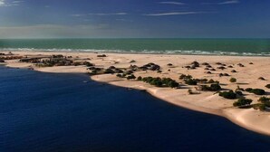 Une vue aérienne d’une zone côtière avec des plages de sable, des cabanes dispersées et une mer d’un bleu limpide.
