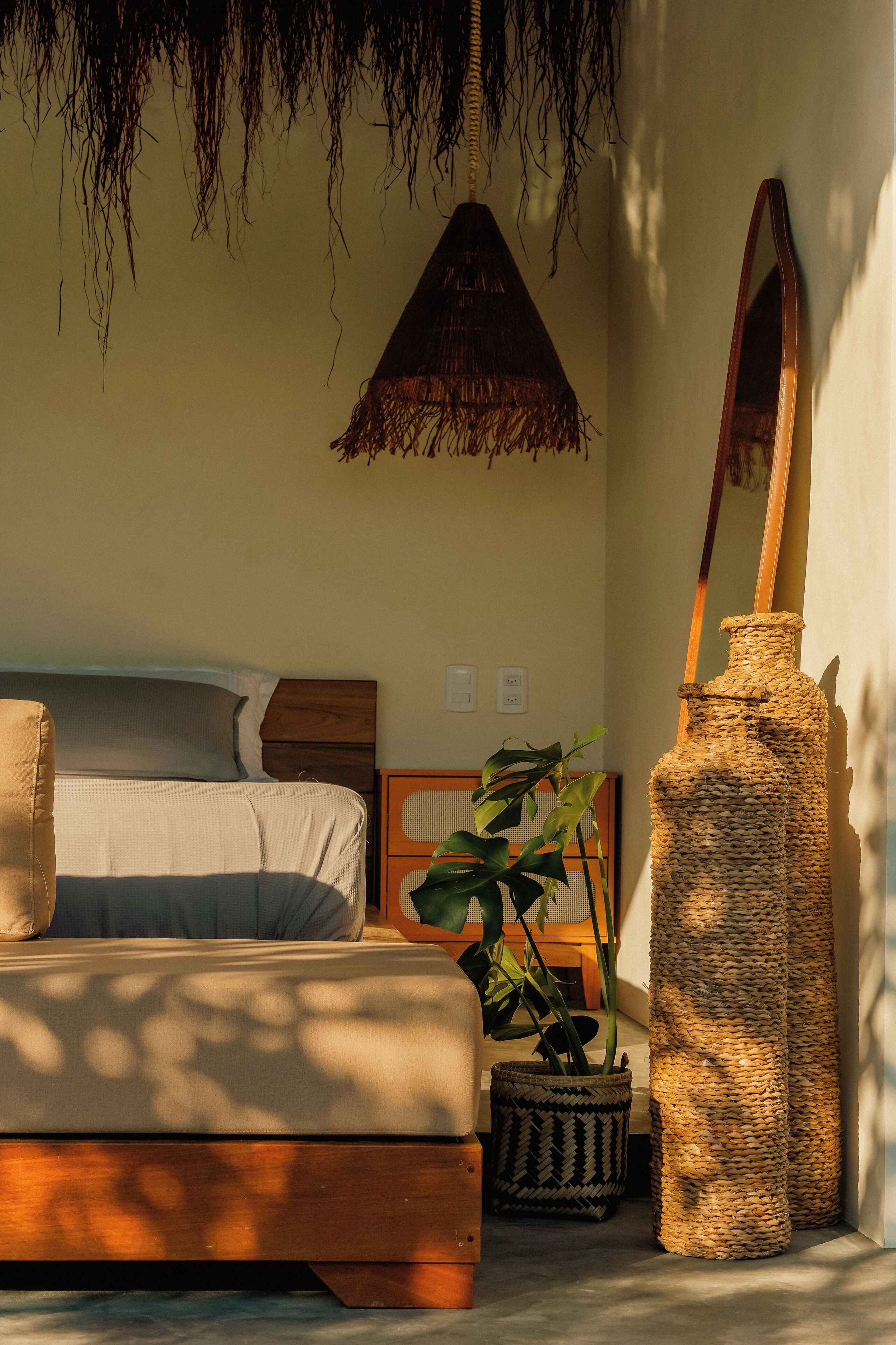 Un dormitorio con cama, espejo, jarra tejida y planta en maceta.