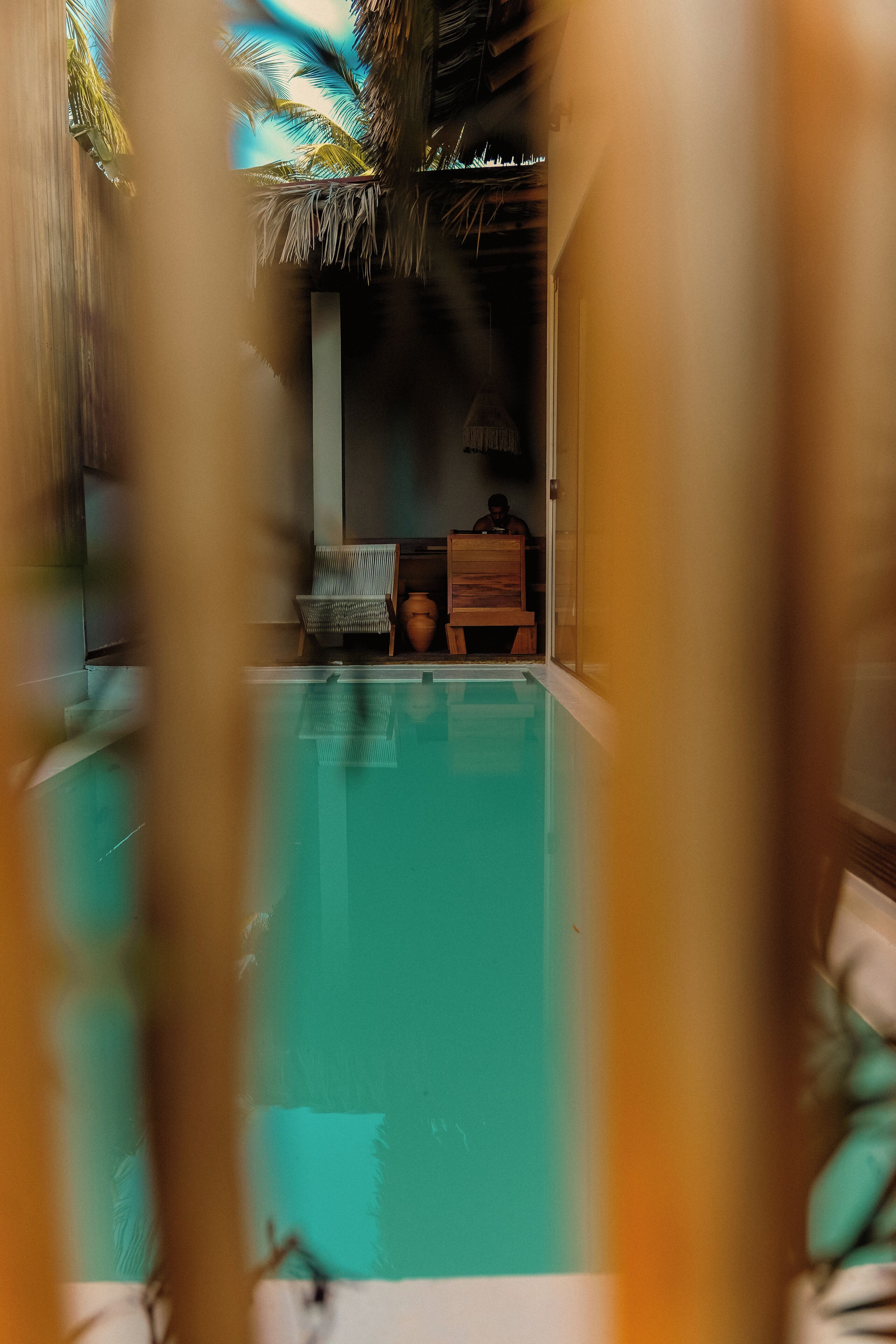 A pool area with a clear view of the water, a wooden bench, and a thatched roof structure.