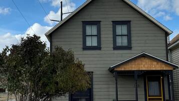 A two-story house with a front porch, a small tree, and a clear sky.