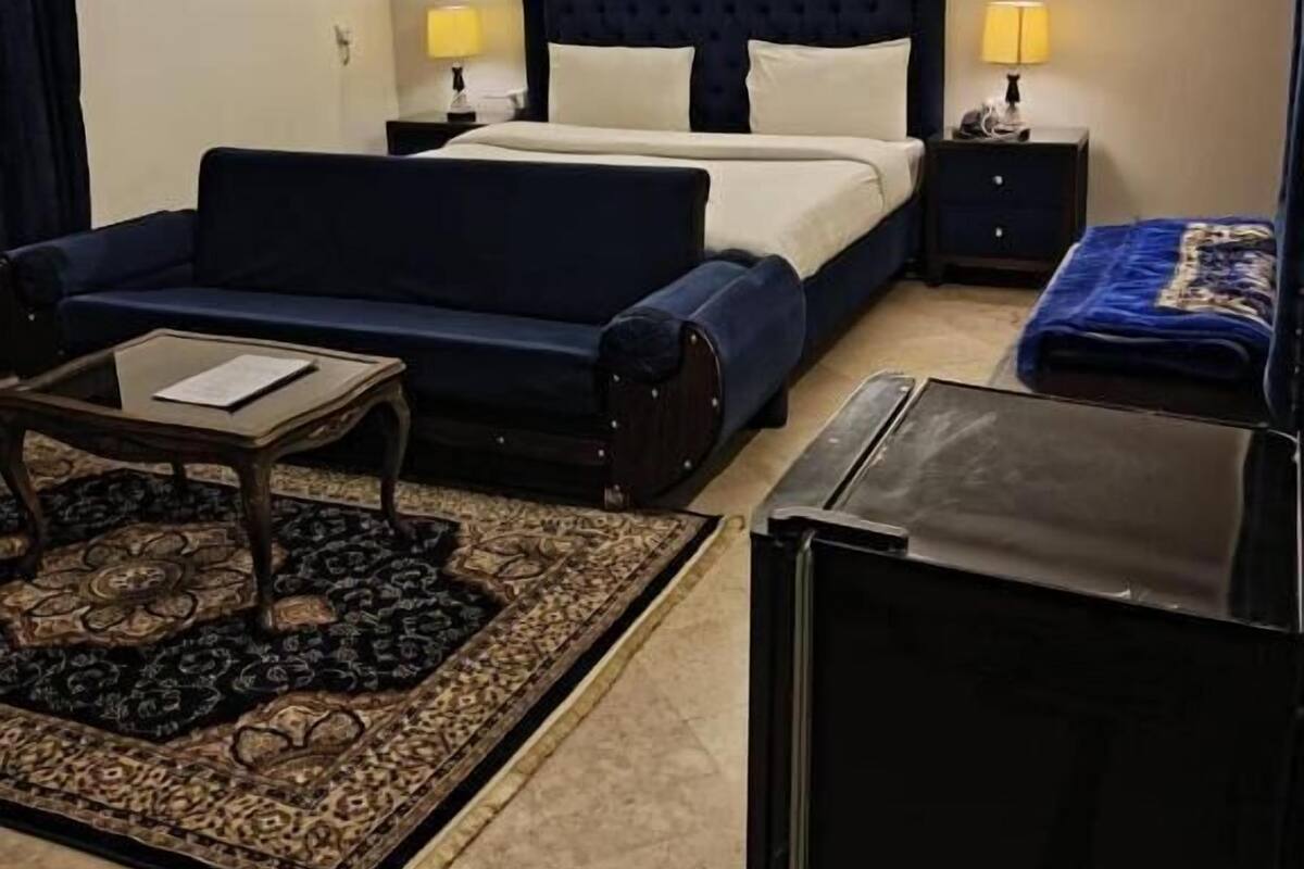 A hotel room with a bed, a sofa, a small table, a TV, and a ceiling fan.