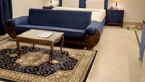 A bedroom with a bed, a sofa, a small table, two bedside tables with lamps, and a patterned rug. - Infinity Villa (Islamabad)