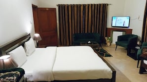 A hotel room with a bed, a television, a desk, a chair, and a curtain. - Infinity Villa (Islamabad)