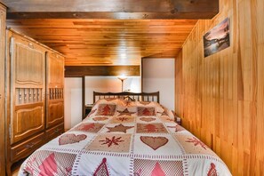 Um quarto com teto de madeira, uma cama com colcha estampada e uma mesa de cabeceira.