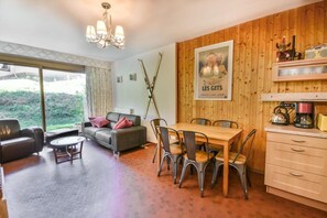A cozy living room with a sofa, coffee table, and dining table with chairs. There's a wooden wall with a poster and a radio. - 1st floor, balcony, 57m², Les Gets (Les Gets)