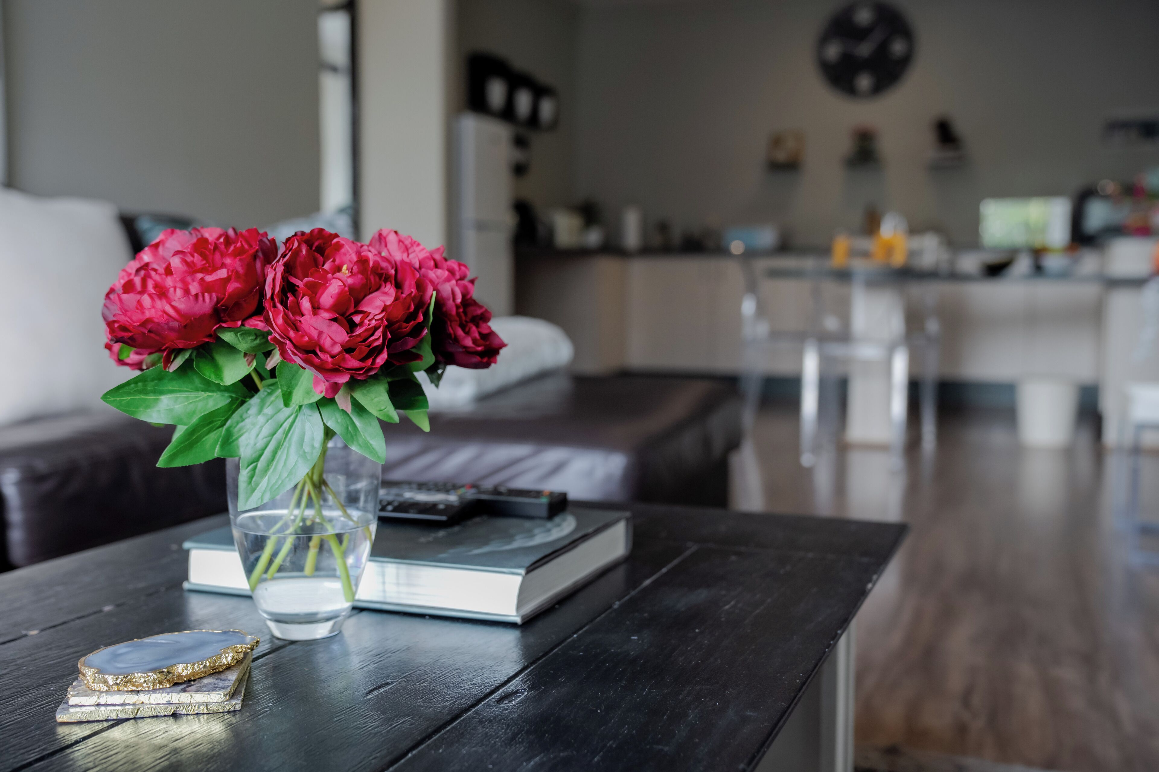 A modern living room with a dark wooden coffee table, a vase with red flowers, a book, and a remote control.