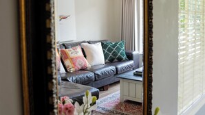 A room with a large ornate mirror reflecting a living area with a sofa, pillows, and a ceiling fan. - Crown Loft - Bright, Airy Stay with Balcony View (Sandton)