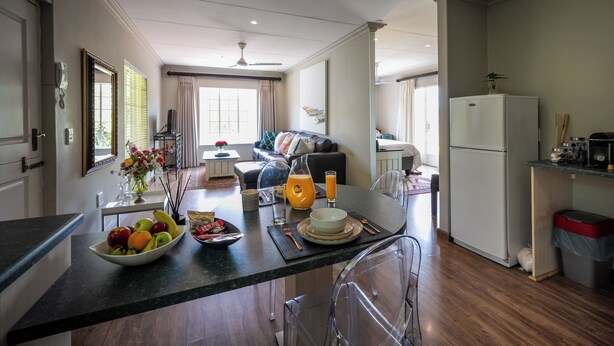 A modern kitchen with a dining area, featuring a central island with a fruit bowl, a coffee maker, and a glass of orange juice. - Crown Loft - Bright, Airy Stay with Balcony View (Sandton)