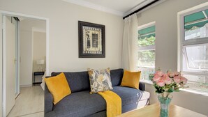 Un salon moderne avec un canapé gris, un plaid jaune et un vase rempli de fleurs roses.