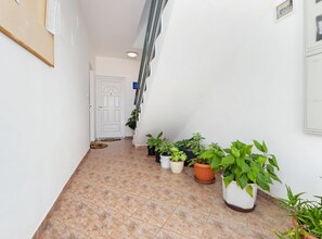 A hallway with a tiled floor, white walls, and a white door at the end. There are several potted plants along the wall. - Brigth and Breezy Rovinj Apartments (Rovinj)