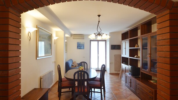 Un coin repas agrémenté d’une arche en briques, d’une table ronde entourée de chaises, d’un ventilateur de plafond et d’un meuble avec des portes en verre.