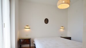 Une chambre à coucher avec un lit, deux tables de chevet, une lampe fixée au mur et un petit tableau.