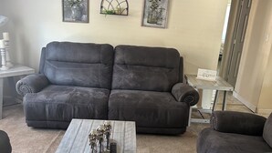 A living room with a gray sectional sofa, a white coffee table, and two wall-mounted decorative items. - Workers Heaven (Daleville)