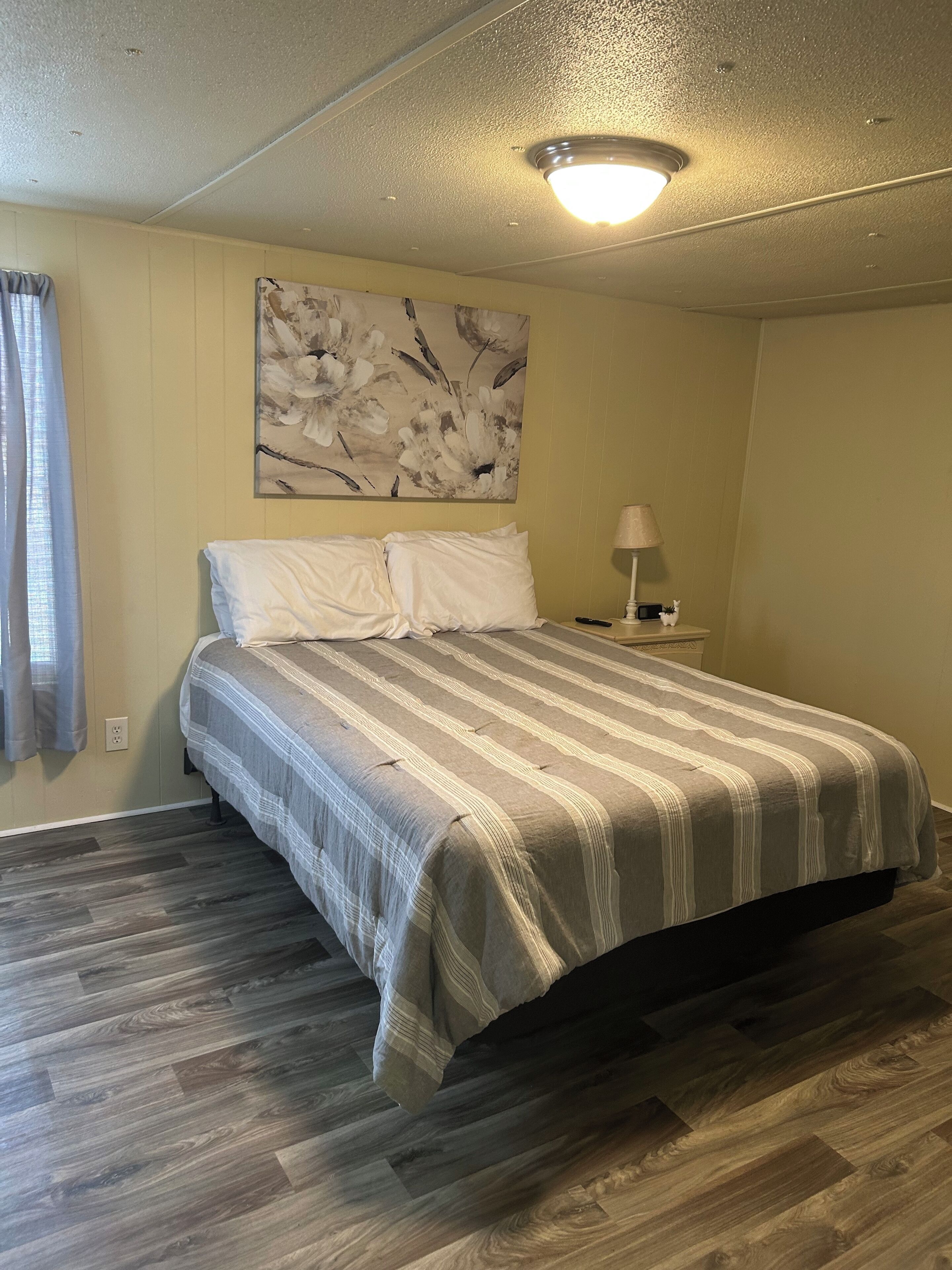 A bedroom with a bed, a nightstand, a lamp, and a floral artwork on the wall.