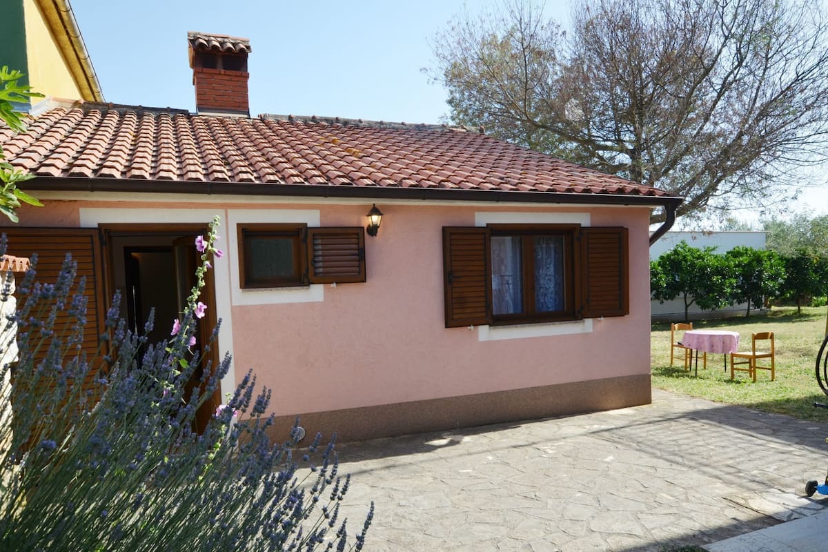 A single-story house with a tiled roof, a small porch, and a table with chairs outside.