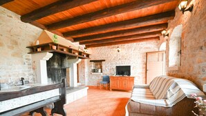 A rustic interior with a stone wall, wooden beams, a fireplace, a television, and a sofa. - Green and Lush Apartments With Terrace (Rovinj)