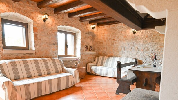 A rustic stone-walled room with two striped sofas, a wooden table with wine glasses, and a stone bench. - Green and Lush Apartments With Terrace (Rovinj)