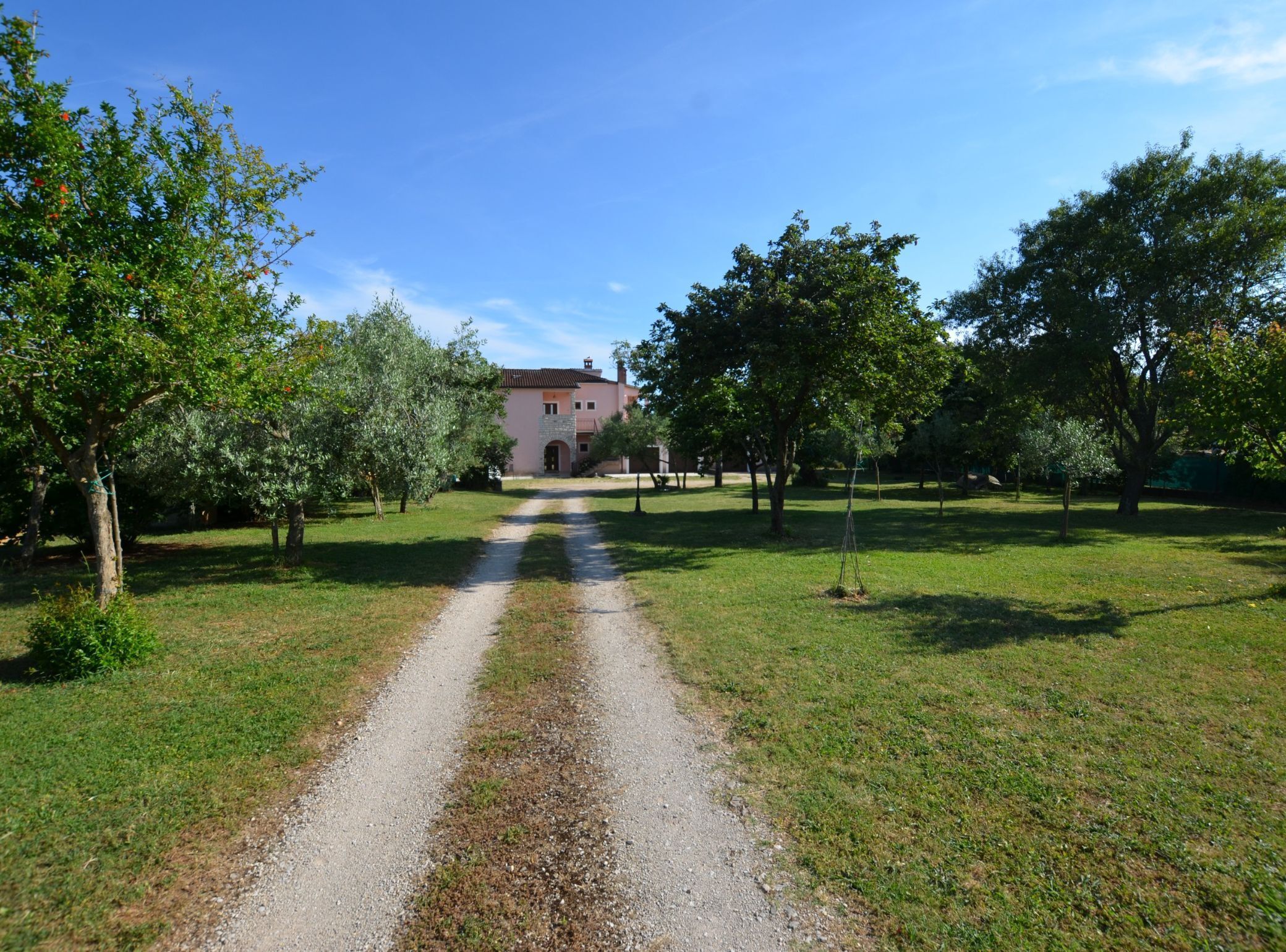 Ein Kiesweg führt zu einem Gebäude mit einer Steinaußenwand und einem Ziegeldach, umgeben von Bäumen und Gras.