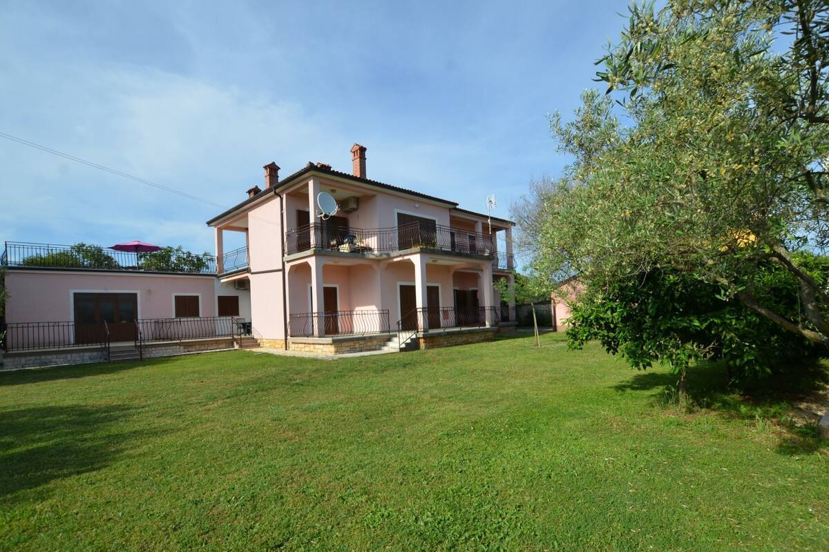 A two-story house with a balcony, a small garden, and a tree.