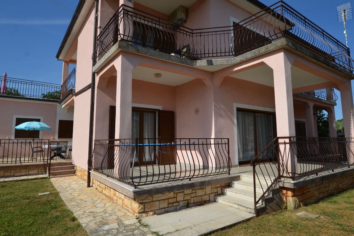 A two-story building with a balcony, stone steps, and a small outdoor seating area.